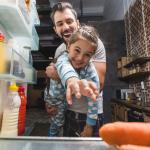 View from inside of a refrigerator as a parent and child reach for food.