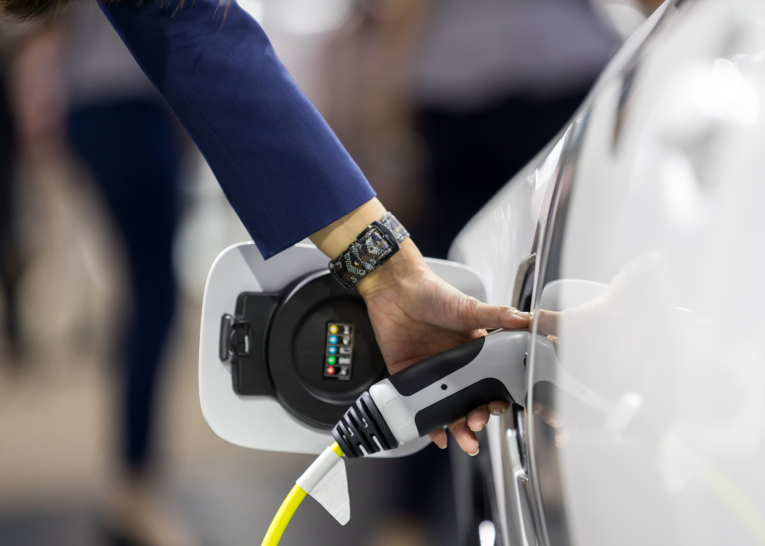 A woman is placing a charge plug into the charge port of a white electric vehicle.