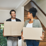 A young couple is carrying cardboard boxes into their new home.