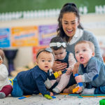 Infants and a caretaker sitting on a rug in a daycare facility