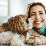 Dog licking face of owner who is smiling and wearing a blue-green top.