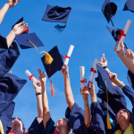 Students at a high school graduation holding diplomas and throwing graduation caps 