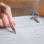 A rental agreement form that a landlord is resting a pen against to show details to a presumed tenant