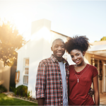 A young Black couple standing outside a home