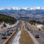 A sunny winter day view of busy Interstate Highway I-70 near Denver, with snow-capped high peaks of Continental Divide towering at west.