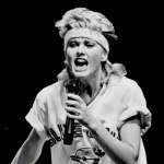 Olivia Newton-John wearing a sports jersey and a headband, performing her hit song "Physical" live at the CNE Grandstand in Toronto, Canada, circa 1982