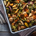 Top shot of a sheet pan filled with chicken and a variety of vegetables, next to a salad bowl