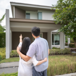 A couple in front of a house, the woman pointing up toward it