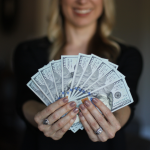 A woman holds up a fan of $100 bills