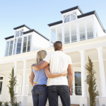 A young couple stands in front of a white two-story house