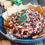 Thanksgiving cheese ball with cranberries and nuts surrounded by crackers in a bowl.