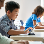 Focused Asian school boy using digital tablet at class in classroom.