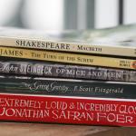 Classic novels including Shakespeare's 'Macbeth,' John Steinbeck's 'Of Mice and Men,' and F. Scott Fitzgerald's 'The Great Gatsby,' on a wooden shelf.