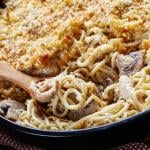 Close-up of roasted turkey tetrazzini with mushrooms and a breadcrumb crust in a black cast-iron skillet with a wooden spoon.