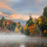 A foggy lake at sunrise surrounded by autumn foliage in Stowe, Vermont