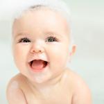 Baby smiling with big blue eyes and bubbles on their head.