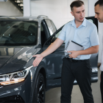 Car salesperson standing next to a black sedan convincing a client to purchase the car