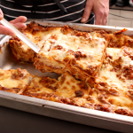 Person's hands cutting out a slice of lasagne from a baking pan