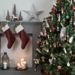 A Christmas tree stands beside a fireplace decorated with stockings