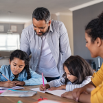 A couple help their two children with their studies, seated at dining room table