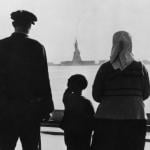 Rear view of an immigrant family on Ellis Island looking across New York Harbor at the Statue of Liberty in the 1930s.