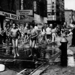 Chief of Police Kennedy opens up a fire hydrant, spraying water over children playing in Hester Street, a designated 'play street' closed to traffic, during the hot New York summer of 1960. 