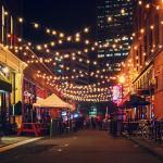 nightlife scene of a street with storefronts and a market in the distance