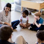 elementary school students sitting in a circle talking to teacher