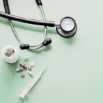 A stethoscope and some pills and a syringe against a clean background