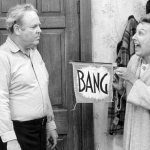 Actor Jean Staplton playing Edith holding a sign with the word "bang" in an attempt to cheer up  Archie, played by Carrol O'Connor, in an episode of 'All In The Family'