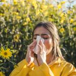 Person sneezes into a tissue due to allergies while surrounded by flowers.