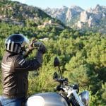 motorcyclist taking photos of scenery by side of the road, mountains and greenery