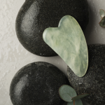 jade color gua sha tool displayed on black stones