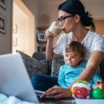 Mom with a baby drinking coffee while working at home with a laptop