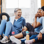 Three older women sitting on a gym floor and laughing