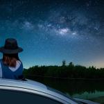 person viewing night sky full of stars by standing up in sunroof 