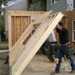two people raising the plywood frame where a wall will go up during a home addition