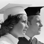 Close-up of two college graduates wearing a white and black cap and gown respectively and looking off into the distance, circa 1970s