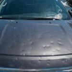 Black car with dents after a hail storm