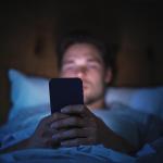 A man browsing on a smartphone while lying in bed at night.