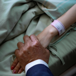A loved one holds the hand of a patient in hospital bed