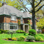 A large two-storey brick and stone house with a well-manicured front lawn in an affluent neighborhood