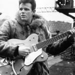 Portrait of rock singer Del Shannon holding guitar.