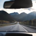 Road trip view of mountains and open road, from behind the wheel in car.