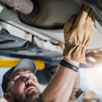 View of underside of car and mechanic checking on catalytic converter.