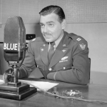US Army Air Corps Capt Clark Gable (1901 - 1960) speaks into a microphone at a desk in a military uniform, 1943
