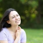 A woman scratching her neck while seated outdoors.