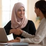 A muslim woman shaking hands with a female professional seemingly in agreement during a discussion.