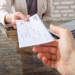 Hand receiving check from business person across table.