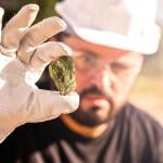 Miner holding gold nugget, with point focus on the gemstone.